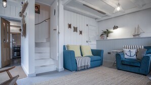 Un soggiorno con un divano blu, una poltrona a dondolo in legno e una scala che conduce a un'altra stanza.