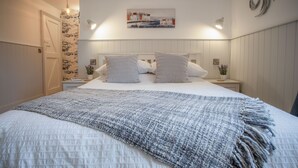 Un letto rifatto con un piumone bianco e due cuscini, una coperta grigia lavorata a maglia, e un quadro appeso alla parete.