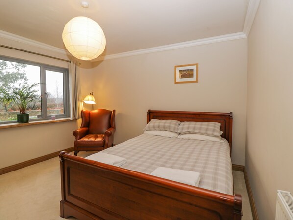A bedroom with a wooden bed, a chair, a lamp, a window, and a framed picture on the wall. - Little Foxes (Calne)