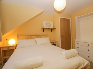 Een slaapkamer met een bed, nachtkastje, lamp en een kledingkast.