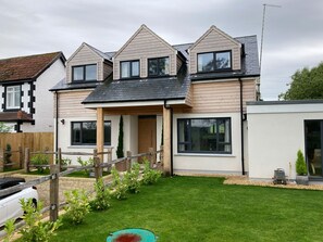 A modern two-story house with a sloped roof, large windows, and a well-maintained lawn. - Little Foxes (Calne)