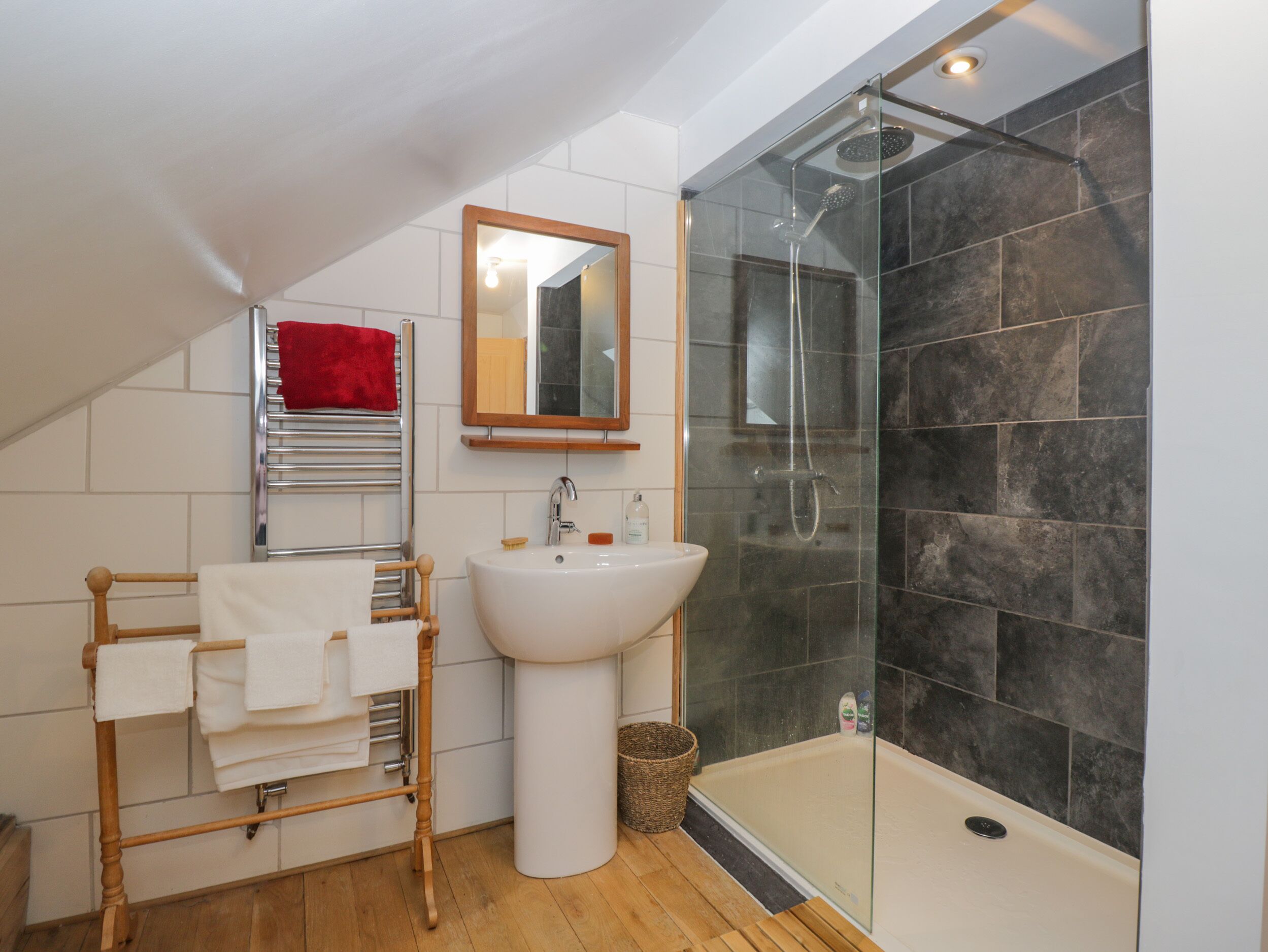 A modern bathroom with a glass-enclosed shower, a white pedestal sink, and a wooden towel rack.