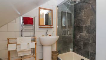 A modern bathroom with a glass-enclosed shower, a white pedestal sink, and a wooden towel rack.