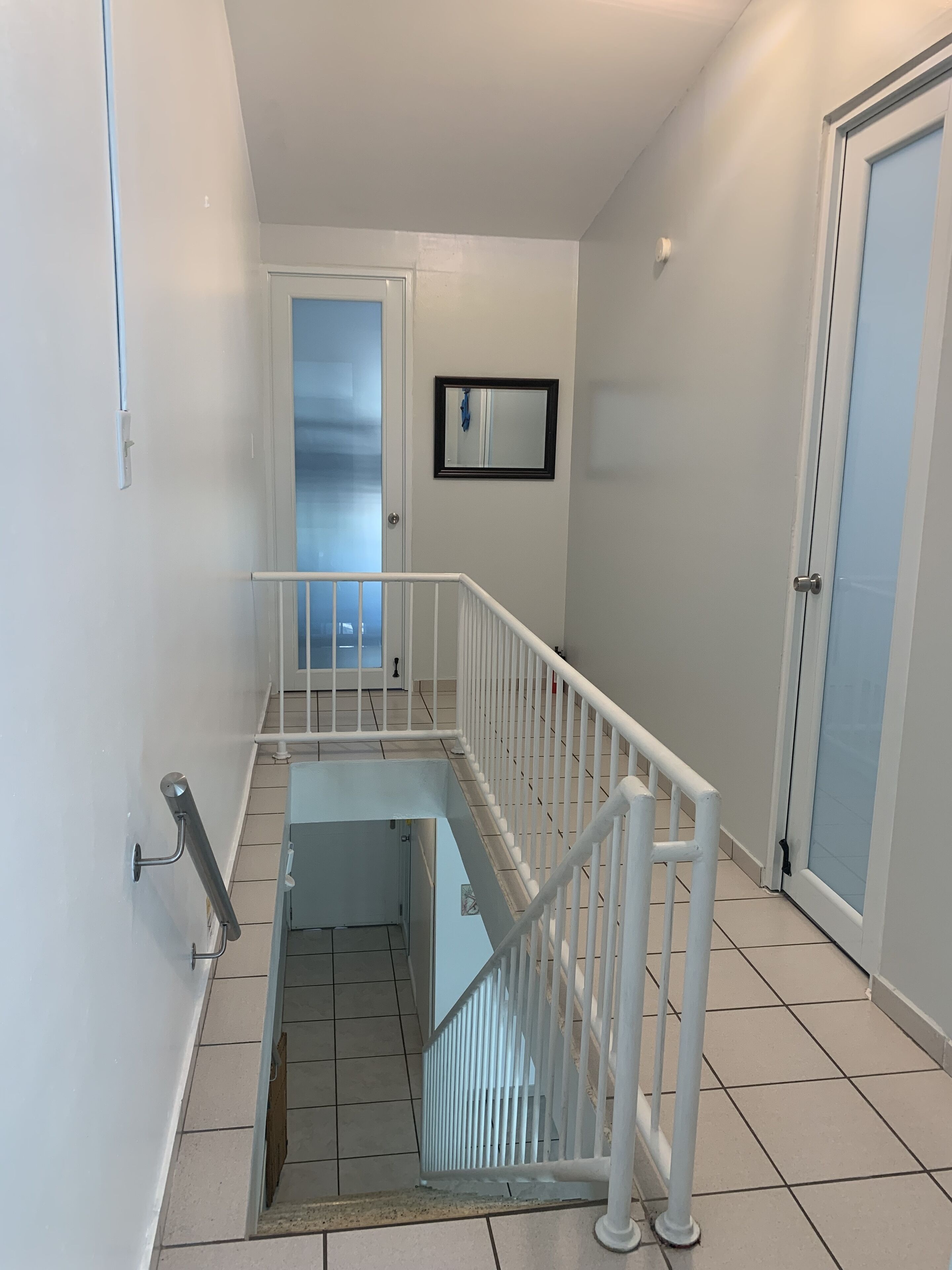 A clean, modern stairwell with white railings and a glass door at the top.