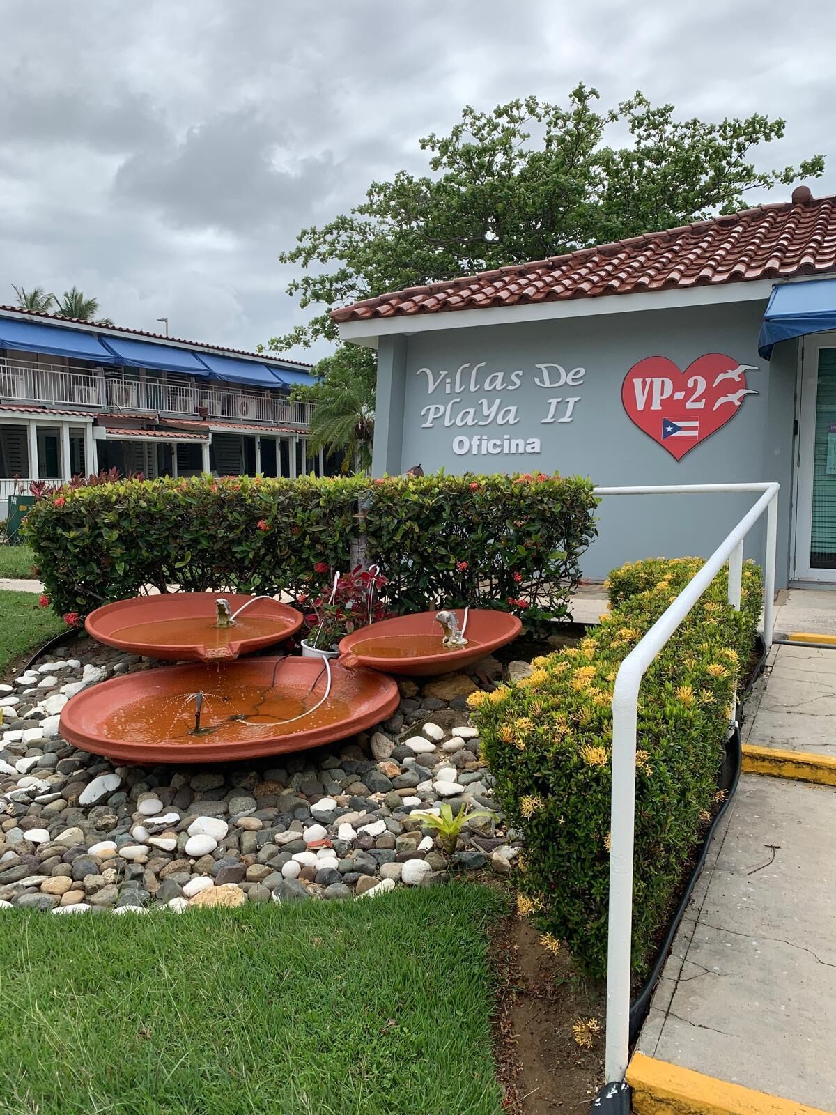 Villas De Playa II Office with a sign, a heart-shaped logo, and a water feature.