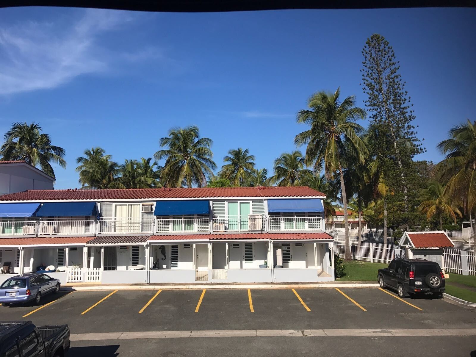 A two-story building with a red-tiled roof, multiple balconies, and a parking lot with yellow lines.
