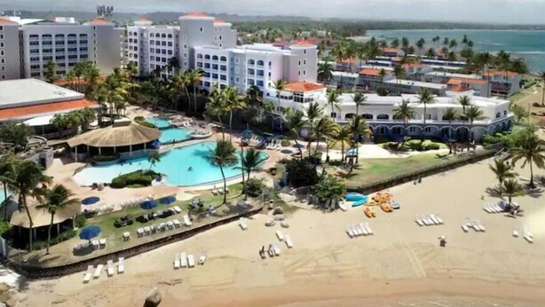 A resort with multiple buildings, a swimming pool, and a beach area with sun loungers.