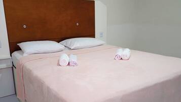 Habitación individual con una cama de madera, almohadas blancas, colcha rosa y dos toallas enrolladas sobre la cama.