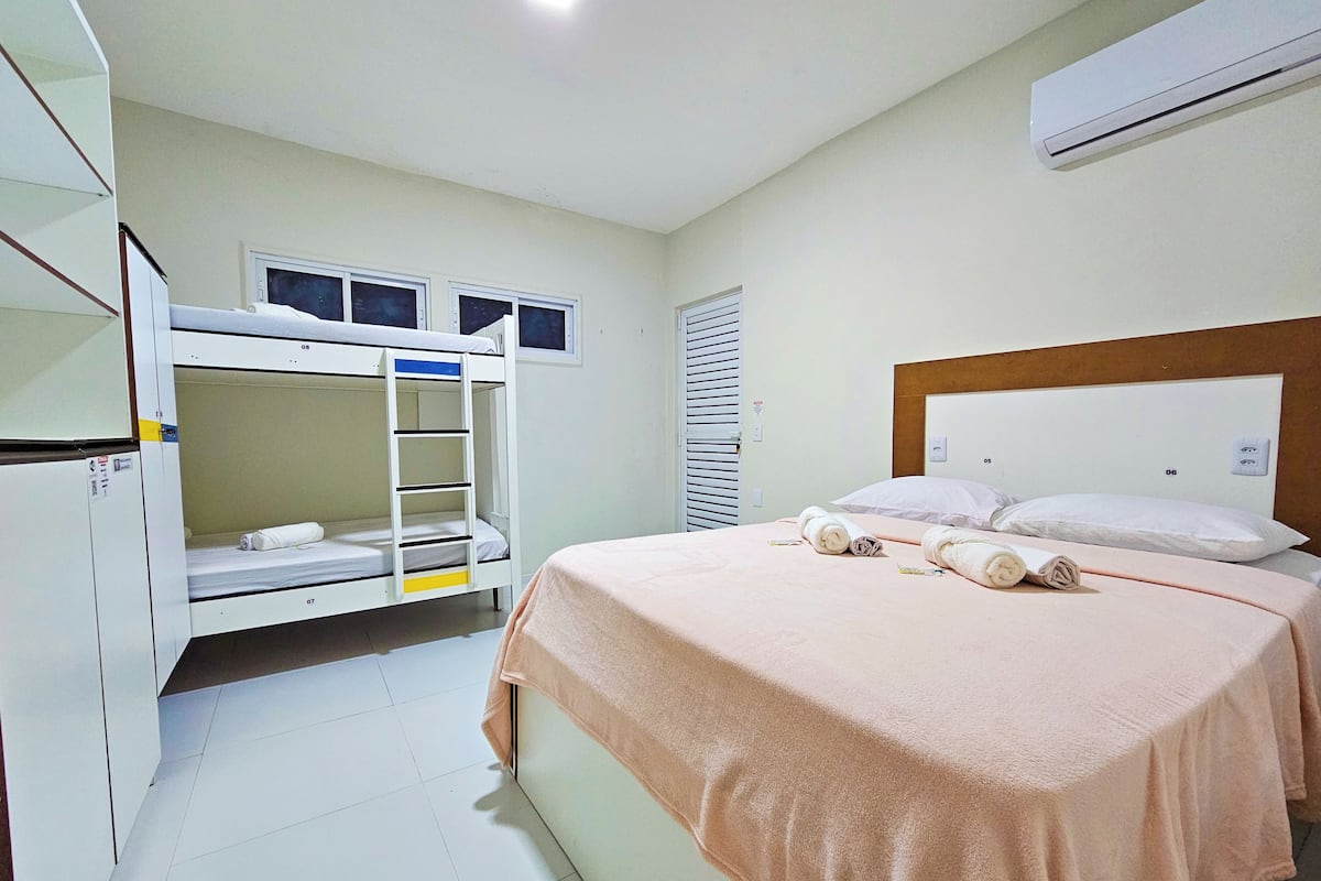 Una habitación de hotel con literas, una cama individual, un armario y un equipo de aire acondicionado.