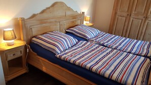 A wooden bed with striped bedding, two bedside lamps, and a nightstand drawer.