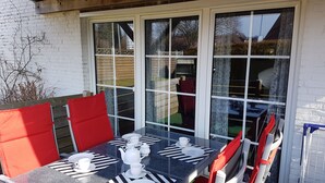 A dining area with a table set for four, a wooden deck, and a white brick wall. - Dornum" vacation apartment (Dornumersiel)