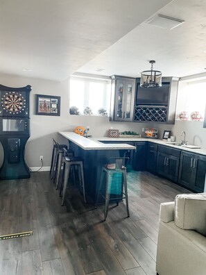 A modern kitchen with a bar area, wooden flooring, and a large window.