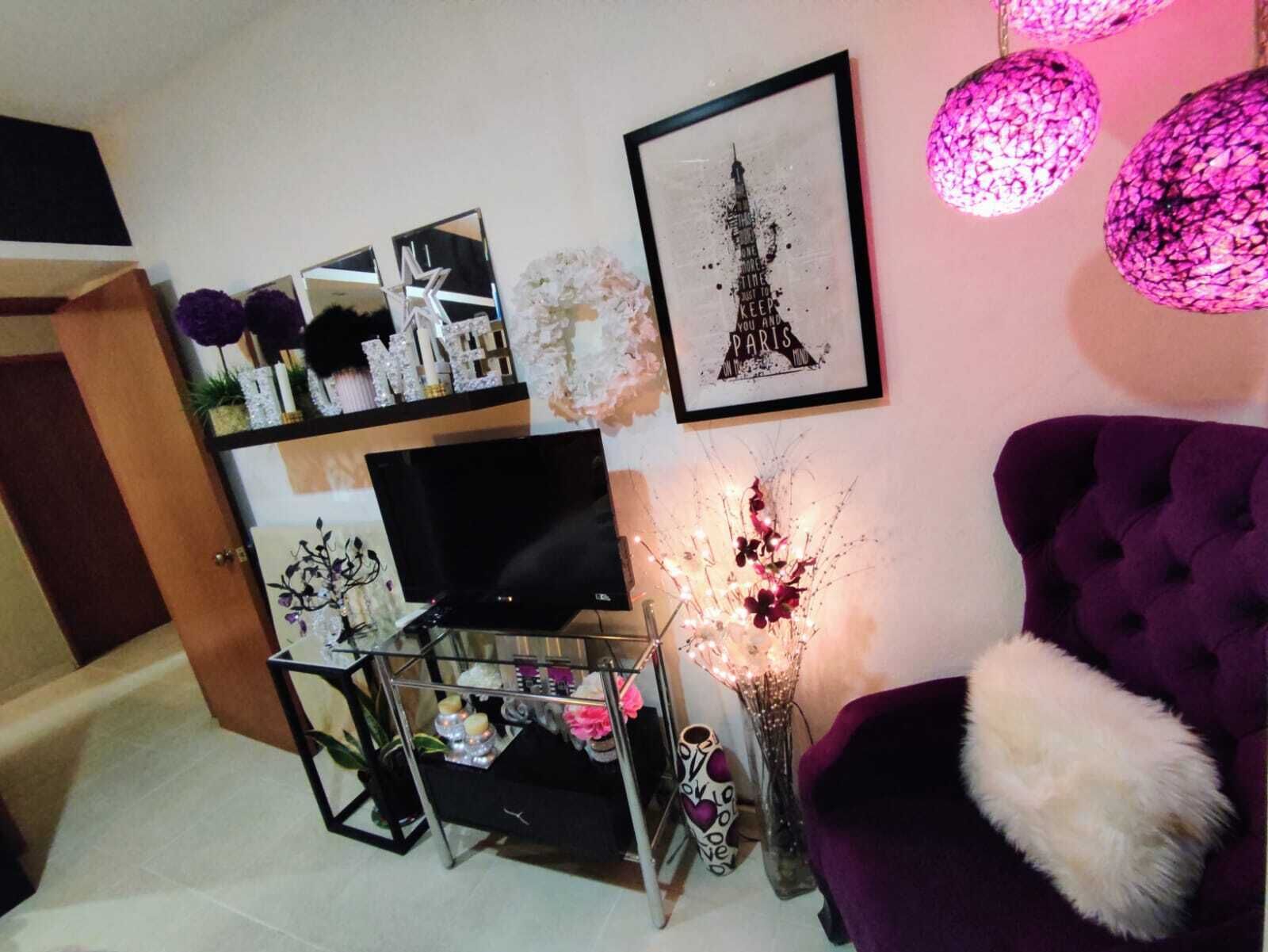 A living room with a purple armchair, a TV, decorative items, and a framed picture of the Eiffel Tower.