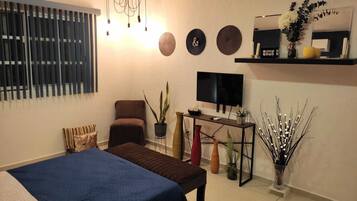 A modern living room with a bed, a TV, a coffee machine, and decorative items.