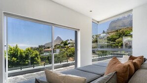 A modern living room with large windows offering a view of a mountain and greenery. - The View CampsBay w/inifinity pool -5 mins from Beach (Cape Town)
