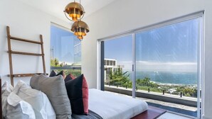 A bedroom with a large window overlooking a coastal view, a wooden ladder, and a modern chandelier. - The View CampsBay w/inifinity pool -5 mins from Beach (Cape Town)