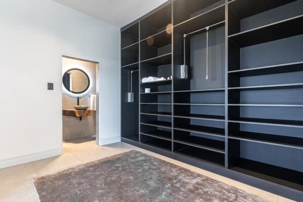 Un placard moderne doté de plusieurs étagères et d’un espace pour suspendre des vêtements, d’un miroir rond et d’un petit coin lavabo.