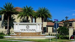 Un edificio con un letrero que dice "The Fountains" y señales de calle que indican Roseville Rd y Woodman Rd.