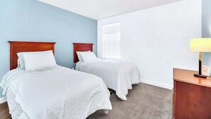 A bedroom with two single beds, a nightstand with a lamp, and a window with blinds. - Big Screen Movie Nights! Champions Gate Resort Close 2 Disney! 8165 (Davenport)