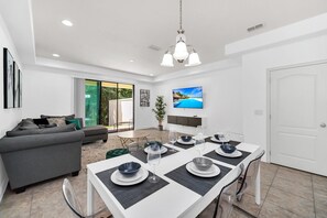 Una sala de estar moderna con comedor, un sofá gris, un televisor montado en la pared y una puerta.
