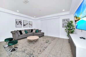 Ein modernes Wohnzimmer mit einem grauen Ecksofa, einem runden Couchtisch und einem großen Flachbildfernseher an der Wand.