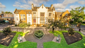 Un bâtiment traditionnel doté d’une façade symétrique, d’une entrée centrale et d’un jardin bien entretenu agrémenté de bancs.