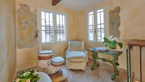 Una stanza con una sedia bianca, un tavolino con un vaso di fiori e uno sgabello decorativo.