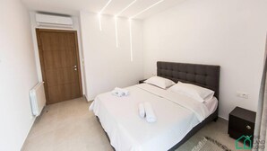 A modern bedroom with a bed, white linens, a wooden door, and a radiator. - Sunset 202 Luxury With gym Club in Lac 1 (Tunis)
