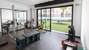 A gym with exercise equipment, a large window, and a view of a tennis court. - Sunset 202 Luxury With gym Club in Lac 1 (Tunis)