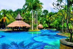 Une piscine bordée de constructions à toits de chaume, le tout entouré d’une végétation tropicale luxuriante.