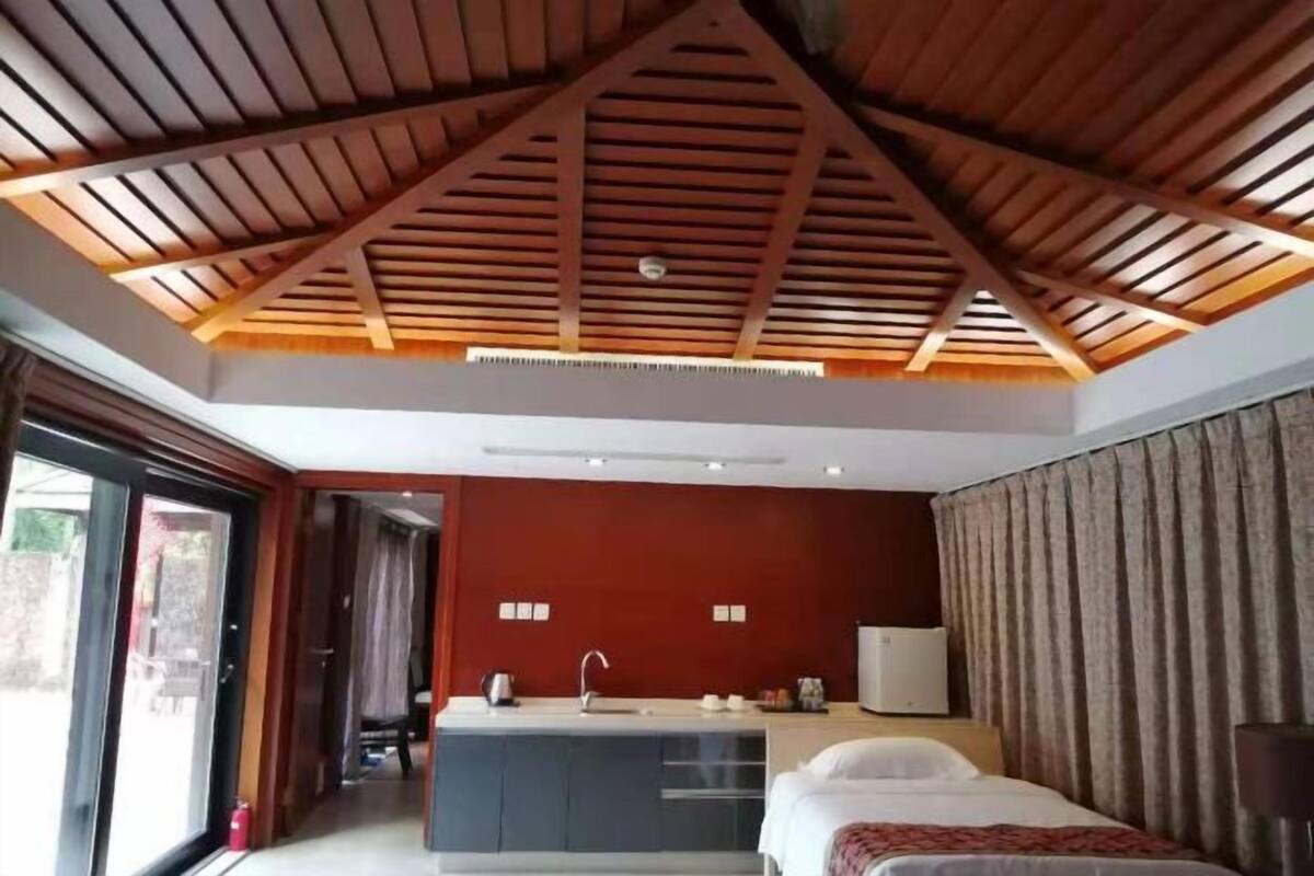 Ein Hotelzimmer mit schräg verlaufender Decke, einem Bett, einer kleinen Küchenzeile und einem großen Fenster.