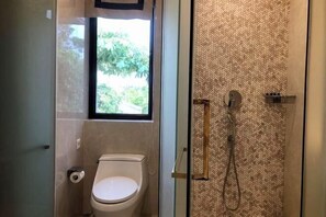 Un baño con inodoro, ducha con pared de patrón espiga y ventana que proporciona luz natural.