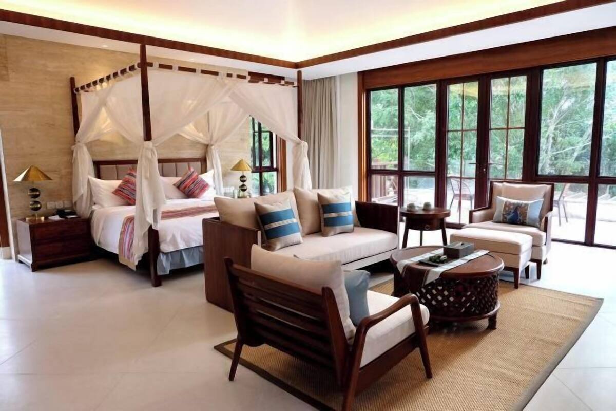 Ein geräumiges Schlafzimmer mit Baldachin, einer Couch, einem Couchtisch und Blick ins Freie durch große Fenster.