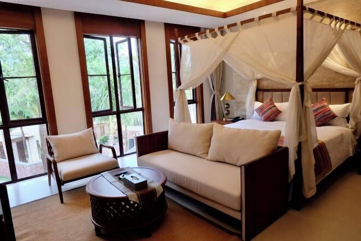 Ein Schlafzimmer mit Himmelbett, einer Couch, einem Sessel und einem kleinen runden Tisch.