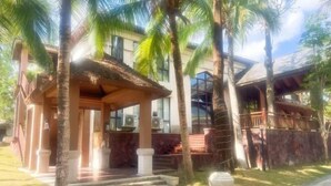 A building with a covered porch, palm trees, and a paved pathway. - Qixianling Zhongnan Hot Spring Apartment Hotel (Baoting)