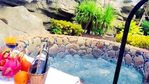 A hot tub surrounded by a stone wall and lush greenery. - Qixianling Zhongnan Hot Spring Apartment Hotel (Baoting)