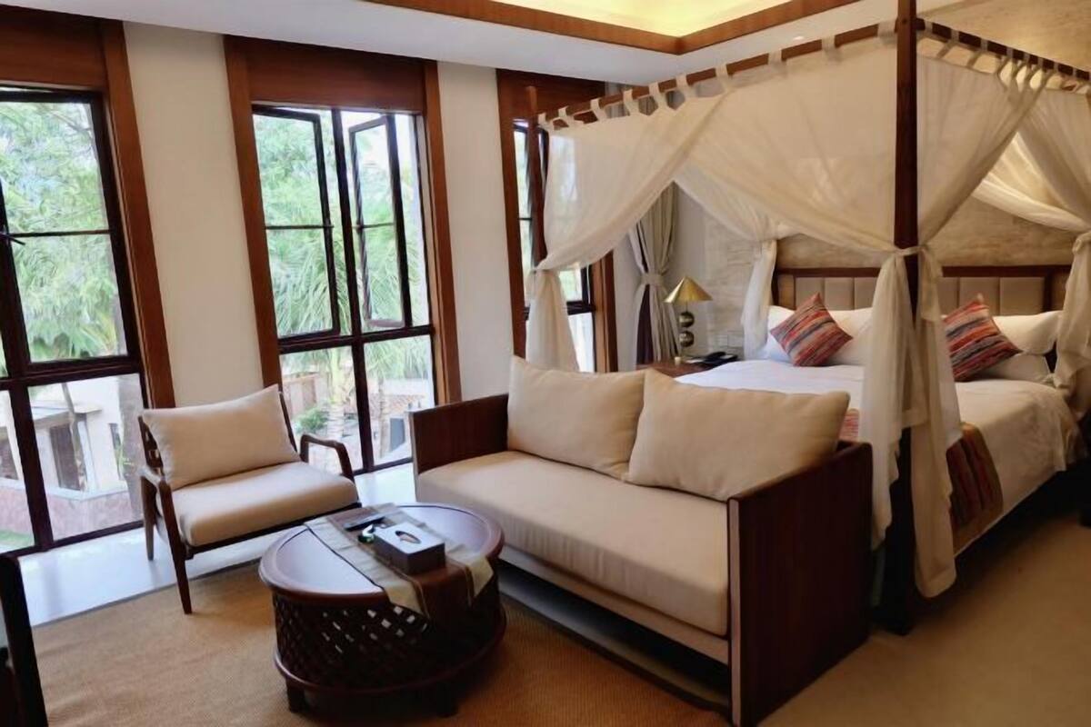 Ein Schlafzimmer mit Himmelbett, einer Couch, einem Sessel und einem kleinen runden Tisch.
