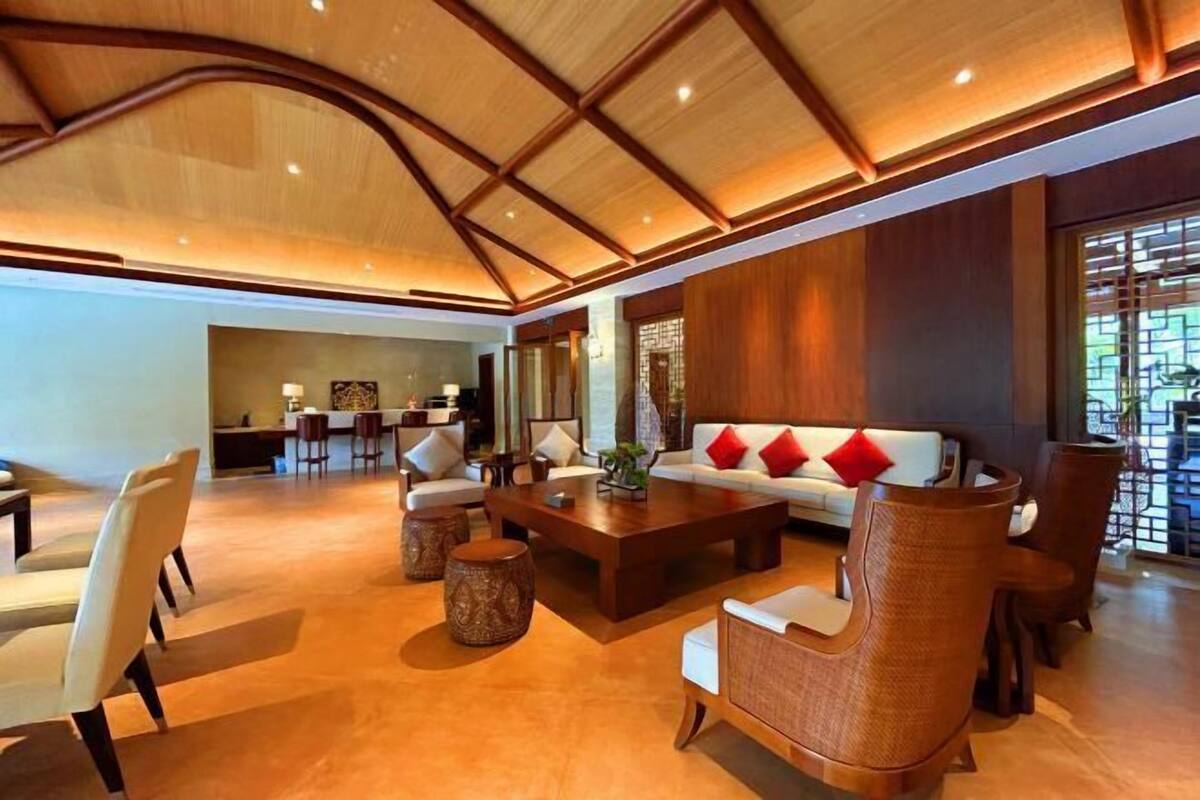 Eine großzügige Lobby mit hoher Decke, einer zentralen Sitzgruppe mit Sofa und Sesseln sowie einem Empfangsschalter im Hintergrund.