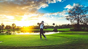Un campo da golf con un giocatore colpend la palla, uno stagno e alberi sullo sfondo.