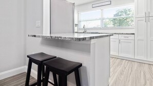 Una cucina con piano di lavoro in granito, mobili bianchi e una finestra con persiane.