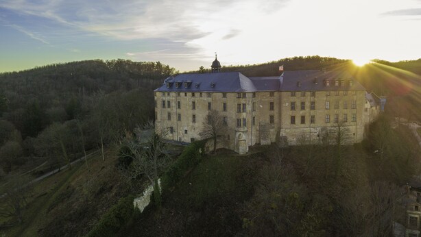 A large, historic building with multiple windows and a prominent tower, surrounded by dense forest and hills. - Harzritter Domizil Großzügige Familienwohnung (Blankenburg OT Cattenstedt)