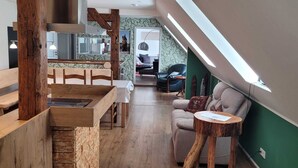 A modern kitchen with a wooden bench, a dining table, and a staircase leading to a bedroom with a bed and a chair. - Harzritter Domizil Großzügige Familienwohnung (Blankenburg OT Cattenstedt)
