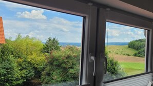 A room with a large window offering a view of a green landscape and a clear sky. - Harzritter Domizil Großzügige Familienwohnung (Blankenburg OT Cattenstedt)
