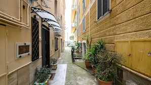 A narrow alleyway with buildings on either side, potted plants, and a small staircase leading to a door.