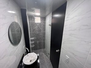 Bathroom features a round mirror, sink with white basin, and shower area.