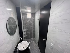 Bathroom features a round mirror, sink with white basin, and shower area.