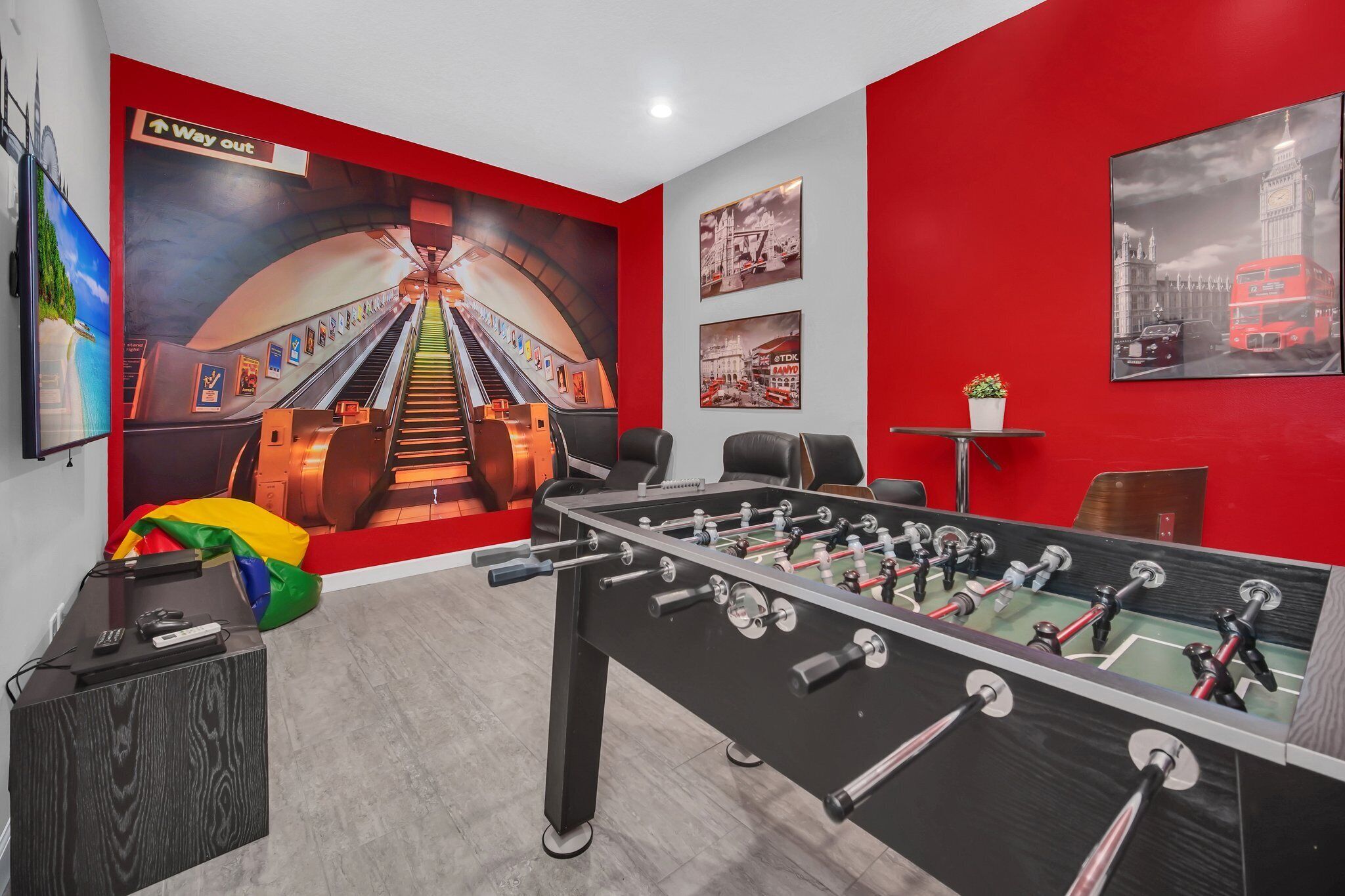 A room with a foosball table, a desk with a computer and phone, a chair, and a wall with a large mural of a train and cityscape.