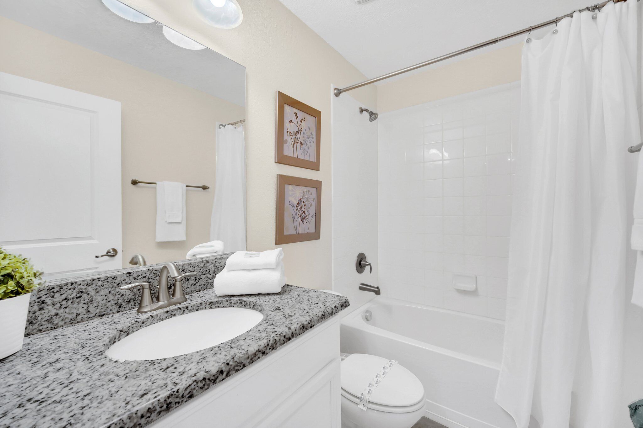 A bathroom with a granite countertop sink, a white toilet, a shower with a glass door, and two framed pictures on the wall.