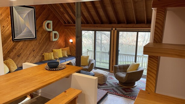 Une pièce chaleureuse avec un plafond en bois, une grande fenêtre et un coin salon agrémenté de coussins.