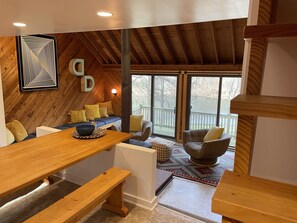 A cozy room with a wooden ceiling, a large window, and a seating area with cushions. - Mid-century A-frame style cabin with lake views near the heart of Amish Country (Stone Creek)